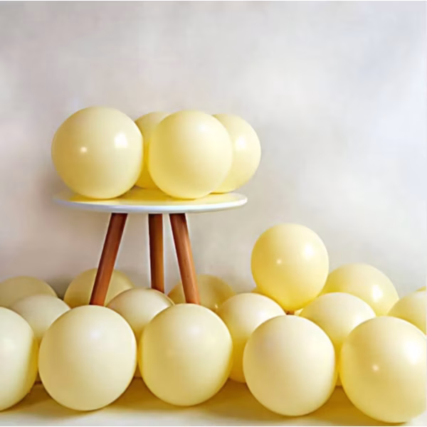 Un grup de baloane din latex umflate, prezentând o nuanță caldă și delicată de galben pastel opac, specifică stilului macarons, aranjate elegant pe o măsuță din lemn și pe podea