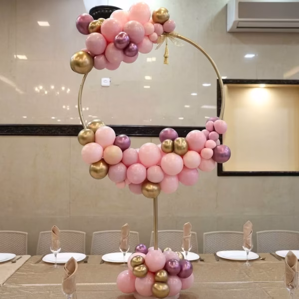Aranjament din baloane roz pudra si auriu chrome montat pe un suport circular asezat elegant in centrul unei mese festive