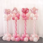 Patru suporturi tip stalp pentru baloane decorate elegant cu baloane din latex roz si albe impletite in spirala pe inaltimea coloanei si baloane din folie in forma de inima si stea asezate in varf