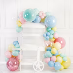 Set Ghirlanda Baloane Macarons Pastel Multicolor Arcada organica din baloane latex in culori pastel tip macarons si baloane bobo transparente asezata pe un carucior decorativ alb de candy bar.