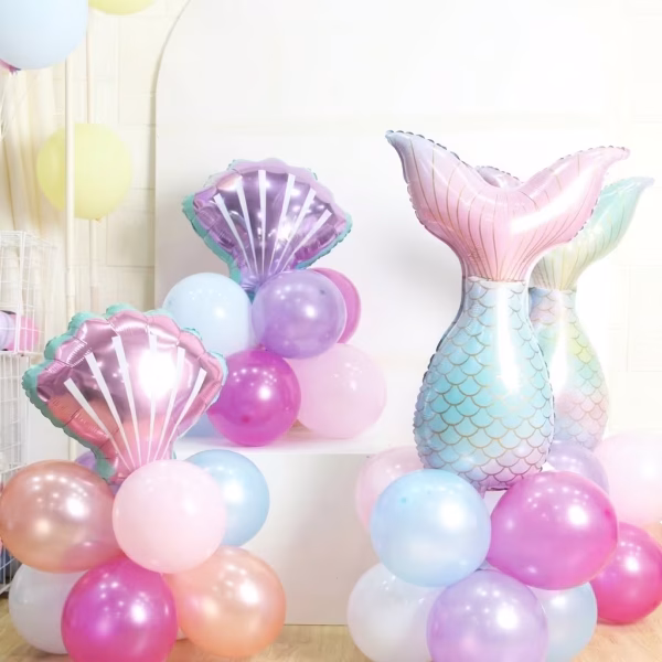 Aranjament decorativ format din 31 de baloane cu tematica Sirena, prezentând la bază clustere din baloane de latex în nuanțe sidefate și pastelate de roz, mov și albastru, peste care tronează două baloane din folie în formă de scoică și două baloane din folie în formă de coadă de sirenă cu detalii solzoase aurii