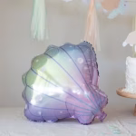 Balon metalizat in forma de scoica marina cu irizatii pastelate mov si verzi, integrat intr-un decor elegant pentru tematica ocean.