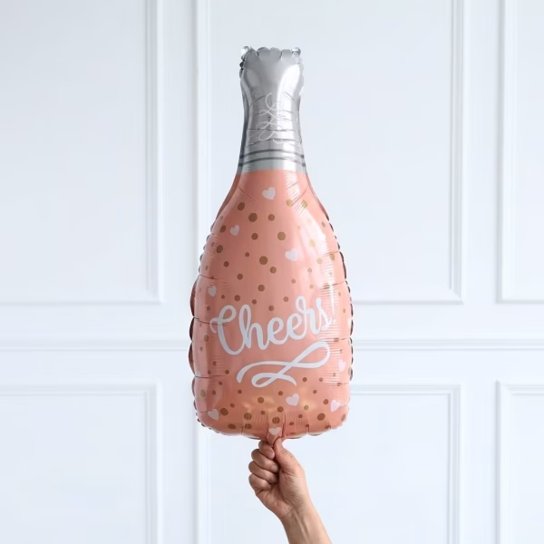 Balon din folie metalizata in forma de sticla de sampanie de culoare roz pudrat decorat cu buline aurii inimioare albe si mesajul central Cheers avand gatul sticlei argintiu