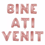Banner format din baloane din folie metalizata de culoare rose gold care formeaza mesajul Bine Ati Venit suspendate elegant pe trei randuri