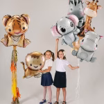Set 6 Baloane Folie Animalute Safari, Design Baby Jungla Set de 6 baloane din folie in forma de pui de animale safari, incluzand un tigru, un leu, un elefant, un hipopotam, o zebra si o girafa, tinute cu bucurie de doua fetite.