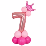 Cifra 7 din folie metalizata rose gold ridicata pe o platforma din baloane latex roz si decorata cu o coronita.