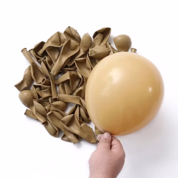 O mana care tine un balon umflat in nuanta bej retro deasupra unei gramezi de baloane neumflate din latex de aceeasi culoare