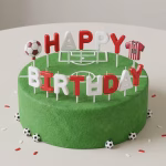 Set 15 Lumanari Happy Birthday Fotbal Lumanari alb-rosii in forma de litere formand Happy Birthday alaturi de o minge si un tricou asezate pe un tort verde tip gazon