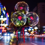 Buchet decorativ format dintr un balon transparent iluminat cu LED uri ce contine un trandafir rosu artificial invelit in hartie neagra si tulle