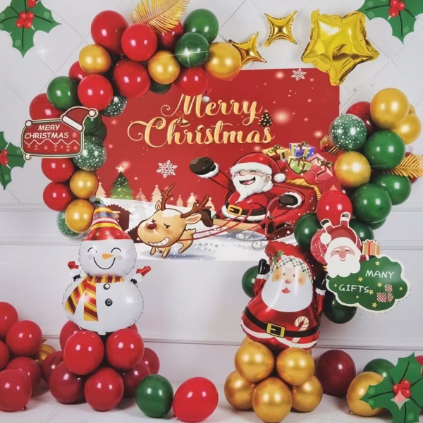 Kit decorativ de Craciun continand un fundal rosu textil cu textul Merry Christmas, incadrat de o arcada organica din baloane rosii, verzi si aurii, figurine din folie reprezentand un om de zapada si pe Mos Craciun, completate de stelute aurii si accesorii din carton