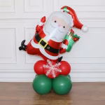 Aranjament festiv format dintr-un balon mare din folie metalizată reprezentându-l pe Moș Crăciun cu un cadou verde, așezat pe o bază construită din baloane din latex în culorile alb, verde închis și roșu