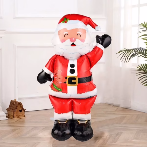 Balon din folie metalizată de dimensiuni gigantice, cu formă 3D de sine stătătoare, înfățișându-l pe Moș Crăciun în costum roșu cu curea neagră, cizme și mănuși negre, având imprimat un mic ren pe haină și salutând cu o mână ridicată
