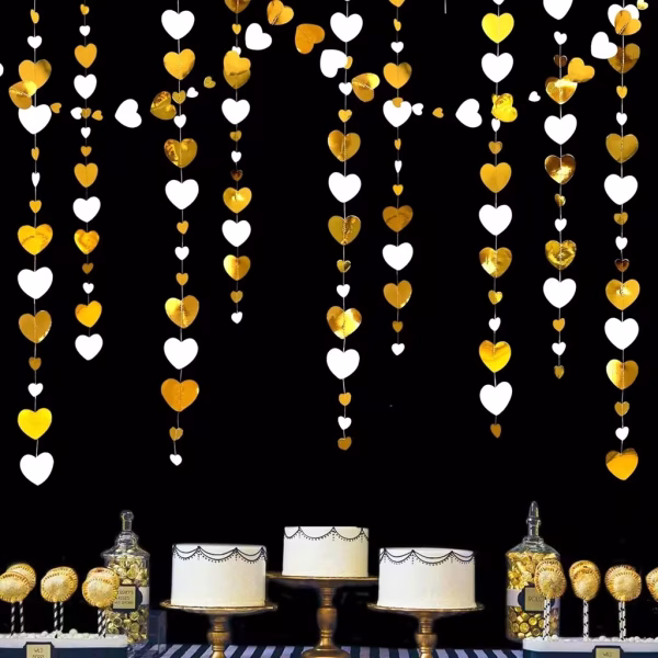 Ghirlande decorative formate din inimioare aurii metalizate si albe suspendate vertical pe un fundal intunecat deasupra unui candy bar cu torturi si prajituri