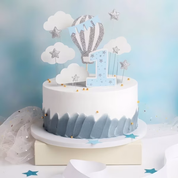 Toppere de tort pentru prima aniversare a unui baiat cu cifra 1 bleu balon cu aer cald argintiu cu bleu norisori albi si stelute sclipitoare asezate pe un tort alb cu baza gri