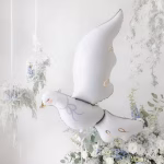 Balon Folie Porumbel Alb Elegant, cu Detalii Aurii, 100x78 cm Balon din folie gigant in forma de porumbel alb elegant, cu detalii aurii si ochi inchisi visatori, plutind intr-un decor floral rafinat de nunta sau botez.