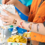 Bratul unui baietel la o petrecere, avand aplicate tatuaje temporare cu masina de pompieri, masina de politie si steaguri de curse auto.