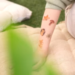 Bratele unor copii avand aplicate tatuaje temporare cu tematica padure, ilustrand o vulpe, o frunza verde, un ursulet si o bufnita.