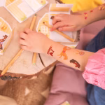 Set 21 Tatuaje Temporare Copii, Tematica Cai si Echitatie Bratul unui copil avand aplicate tatuaje temporare cu caluti si mesajul I love horses, in timp ce deseneaza si se distreaza la o petrecere.