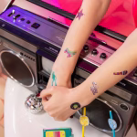 Set 23 Tatuaje Temporare Retro Disco, Decor Petrecere Anii '80 Colectie de 23 de tatuaje temporare cu tematica retro disco, incluzand patine cu rotile, casetofon, cub rubik, siluete de dansatori si textul Dancing Queen.