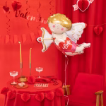 Balon din folie Cupidon umflat cu heliu, plutind deasupra unei mese romantice decorate cu fata de masa rosie, lumanari si un telefon retro.