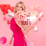 balon folie inima cu sageata O femeie zambitoare tinand in brate un balon din folie in forma de inima rose gold, strapuns de o sageata argintie, cu mesajul Love You.