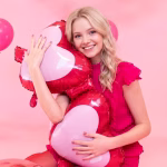 O tanara zambitoare tinand in brate un balon din folie gigant in forma de ochelari cu inimi la o petrecere cu tematica roz.