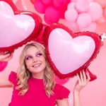 O tanara zambitoare tinand in brate un balon din folie gigant in forma de ochelari cu inimi la o petrecere cu tematica roz.