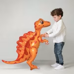 balon folie dinozaur airwalker Un baietel interactionand cu un balon gigant din folie de tip airwalker in forma de dinozaur portocaliu asezat pe podea.