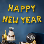 Banner Baloane HAPPY NEW YEAR Auriu 40 cm Decor de Revelion cu litere din baloane folie aurii ce formeaza mesajul Happy New Year deasupra unui tort festiv si a unui balon negru.