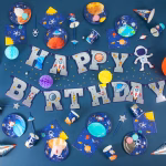 O masa festiva decorata complet in tematica spatiului cosmic, incluzand farfurii, pahare, servetele si un banner Happy Birthday.