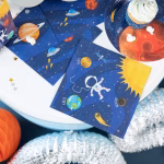 Aranjament festiv pentru o petrecere cu tematica spatiu, incluzand servetele cu astronauti asortate perfect cu farfurii si pahare imprimate cu planete.