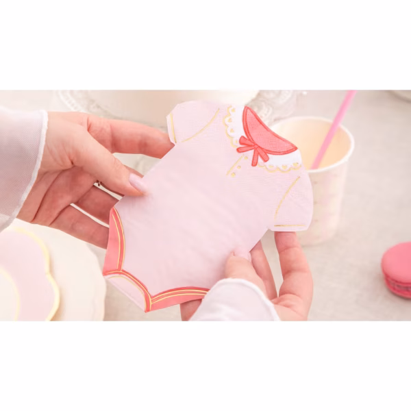 Servetele Forma Body Bebelus Roz O persoana tinand in mana un servetel roz in forma de body bebelus, deasupra unei mese festive, evidentiind dimensiunea si calitatea premium a detaliilor aurii.