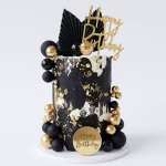 Tort cu textură abstractă în alb și negru, decorat cu stropi de vopsea aurie comestibilă și accesorizat cu un set de bile decorative negre și aurii, alături de frunze evantai.