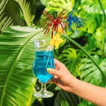 Pahar cu un cocktail albastru și o felie de fruct carambola, decorat festiv cu două bețișoare tip artificii roșu și albastru.