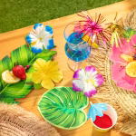 Masă decorată în stil tropical, cu frunze, flori de hibiscus, fructe proaspete și un pahar de cocktail decorat cu bețișoare strălucitoare tip artificii.