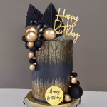 Set 18 Toppere Tort Auriu și Negru Tort negru elegant cu inserții grafice aurii, decorat cu o cascadă voluminoasă de bile aurii și negre, frunze evantai negre și mesaj Happy Birthday auriu.