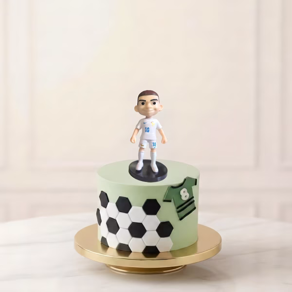 Fotografie de produs ce prezintă o figurină decorativă 3D cu fotbalistul Cristiano Ronaldo, purtând echipamentul de joc cu tricou roșu, detalii verzi și numărul 7. Figurina este așezată stabil prin intermediul unui disc negru deasupra unui tort tematic verde pentru pasionații de fotbal, completat de decorațiuni din pastă de zahăr specifice sportului.