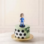 Figurină 3D topper tort cu jucătorul Kylian Mbappe în echipament albastru, decorând un tort tematic cu fotbal.