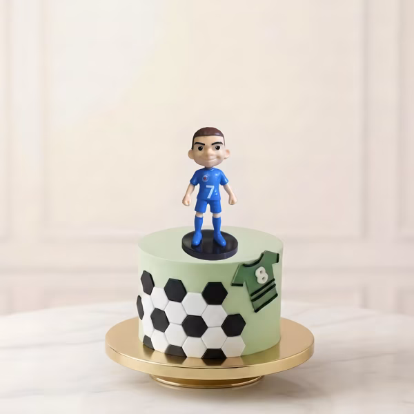 Figurină 3D topper tort cu jucătorul Kylian Mbappe în echipament albastru, decorând un tort tematic cu fotbal.
