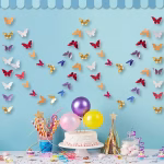 Ghirlanda Banner Fluturi Multicolori 3 Metri Decor de petrecere pe fundal albastru cu un tort accesorizat cu baloane pastelate si o ghirlanda cu fluturi multicolori suspendata in fundal.