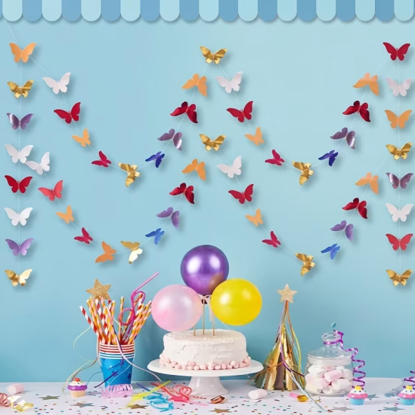 Ghirlanda Banner Fluturi Multicolori 3 Metri Decor de petrecere pe fundal albastru cu un tort accesorizat cu baloane pastelate si o ghirlanda cu fluturi multicolori suspendata in fundal.
