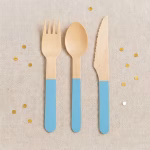 Set 12 Tacamuri Lemn Bleu 16 cm Furculita lingurita si cutit din lemn natur cu maner vopsit in culoarea bleu asezate pe un fundal textil cu confetti.