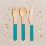 Set 12 Tacamuri Lemn Turcoaz 16 cm Furculita lingurita si cutit din lemn natur cu maner vopsit in culoarea turcoaz asezate pe un fundal textil cu confetti.