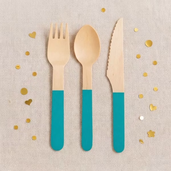 Set 12 Tacamuri Lemn Turcoaz 16 cm Furculita lingurita si cutit din lemn natur cu maner vopsit in culoarea turcoaz asezate pe un fundal textil cu confetti.