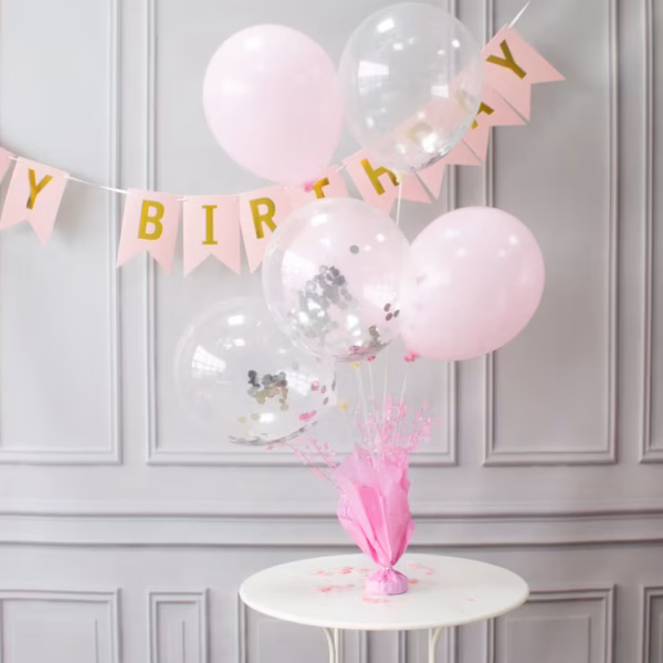 Suport Greutate Baloane Roz cu Betisoare Aranjament festiv pe o masa rotunda alba, folosind un suport cu greutate pentru baloane roz, decorat cu 5 baloane asortate in nuante de roz pastel si transparente cu confetti.