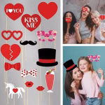 Set 14 Propsuri Foto Party Tematica Iubire Femei si copii zambind si distrandu-se in timp ce folosesc propsuri foto din carton cu inimi si mesaje de iubire la o petrecere.