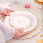 Mâinile unei femei așezând un aranjament format dintr-o farfurie de ceramică și farfuria de carton Sweet Baby roz pal.