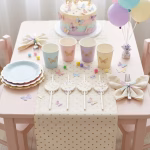 Masa pregatita pentru o petrecere de fetite cu tematica fluturi incluzand paie decorative pahare pastelate farfurii si baloane asortate