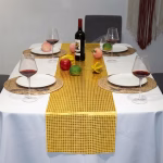 Masa decorata elegant pentru cina cu o traversa din paiete aurii pozitionata central printre farfurii fructe proaspete si o sticla de vin.