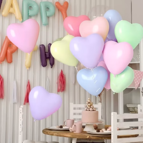 Baloane in forma de inima in culori pastelate umflate cu heliu plutind deasupra unei mese festive decorate pentru o petrecere aniversara